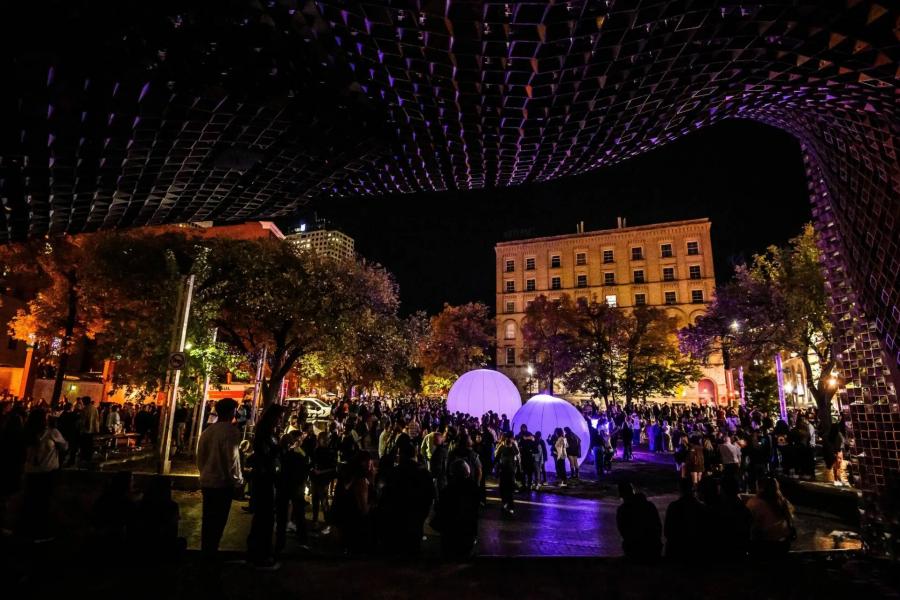 A large crowd gathers under an illuminated installation at night during Nuit Blanche.
