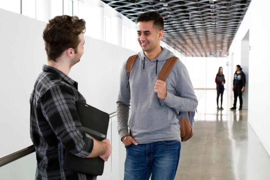 An international graduate student chats with a mentor in a UM hallway.