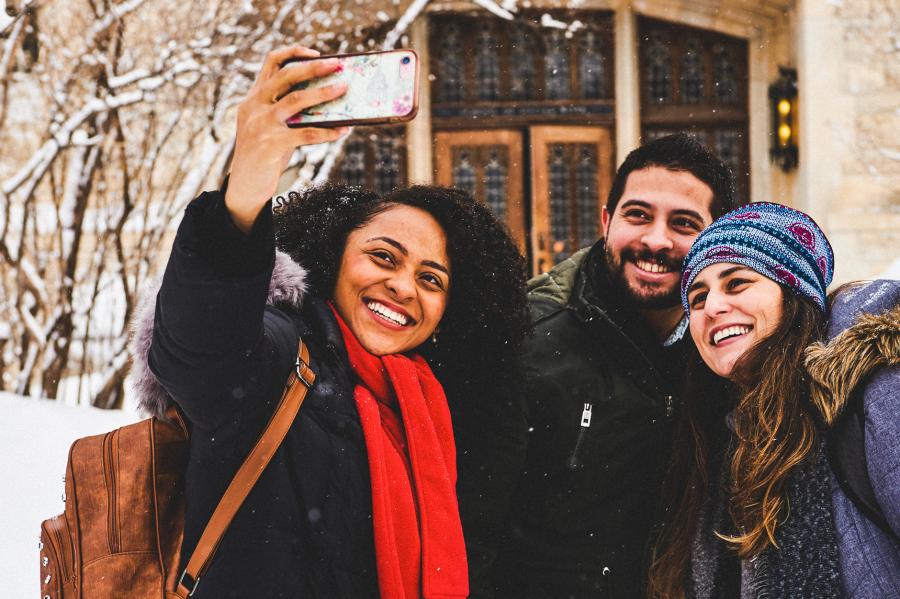 An image of three students outside during winter in front of U.M.'s Buller building, taking a selfie.