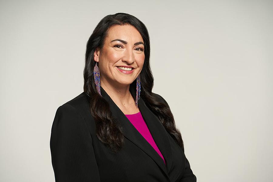 Image of a woman with long black hair in a suit wearing colorful beaded earrings.