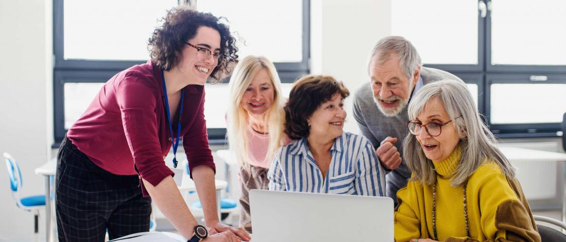 A woman is teaching a group of elderly to use a laptop