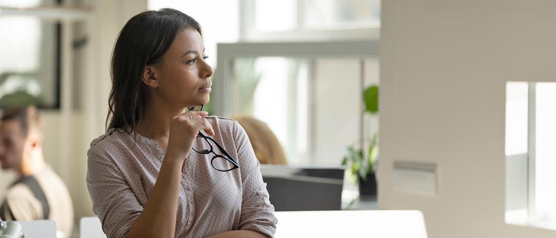 Female worker employee standing at office workplace taking short break in work looking at distance planning future career