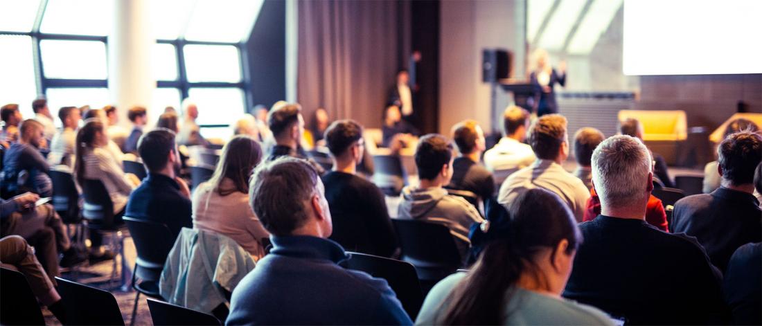 The audience is listening to a speaker in a conference room.