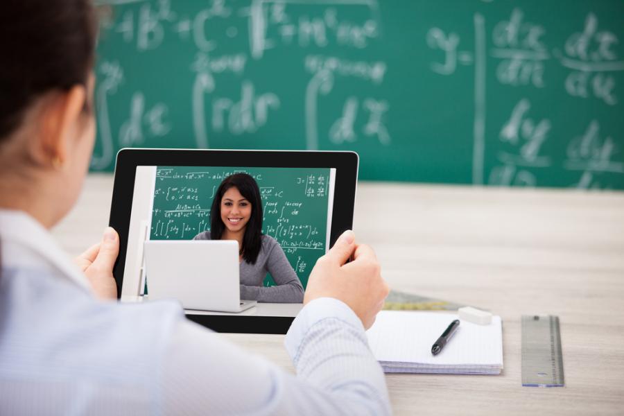 student with tablet, watching instructor at chalkboard