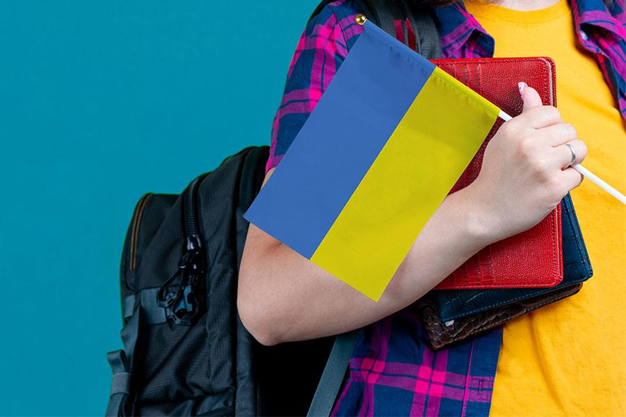 Young girl with school stuff holds in hand Ukraine flag close up