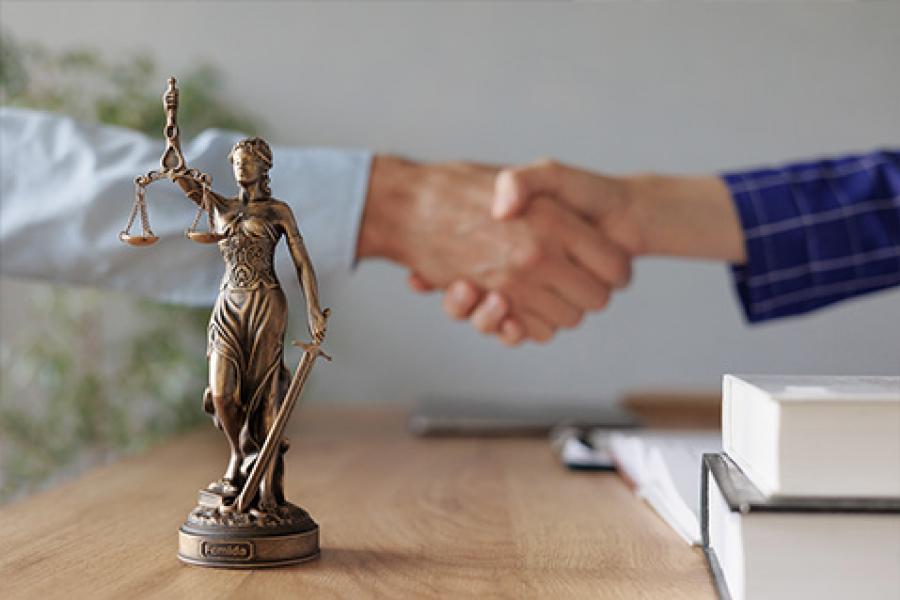 Photo of scales of justice, books, professional handshake.
