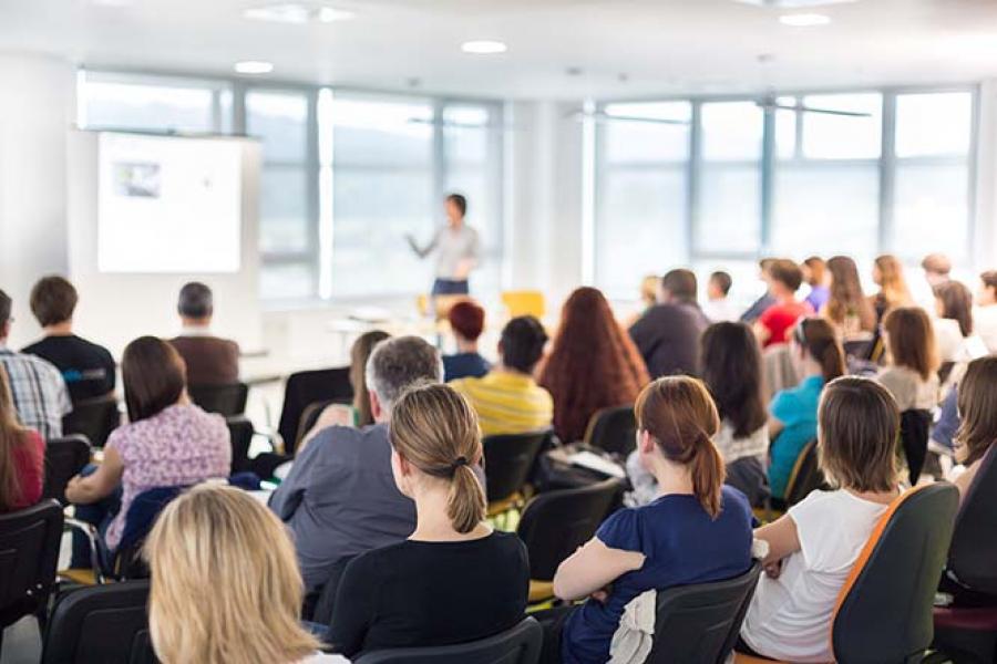 A person presenting to an audience in a bright conference room.