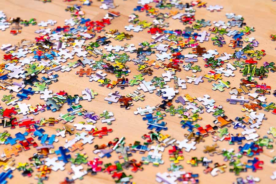 A large number of colorful puzzle pieces are scattered on a light wooden surface.