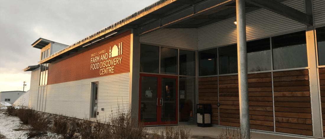 The front of the Bruce D. Campbell Farm and Food Discovery Centre is light by early morning sunlight. There is a list dusting of snow on the ground and small icicles hanging off the roof.
