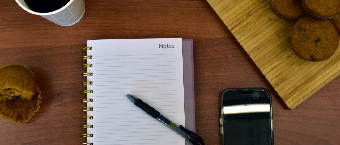 Coffee, muffins, pen and paper plus phone lay on a table