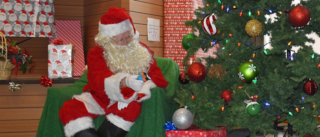 Santa sits by a tree and gives gifts