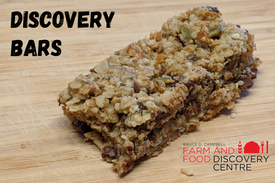 A rustic homemade granola bar sitting on a wooden cutting board with the title "Discovery Bars". 