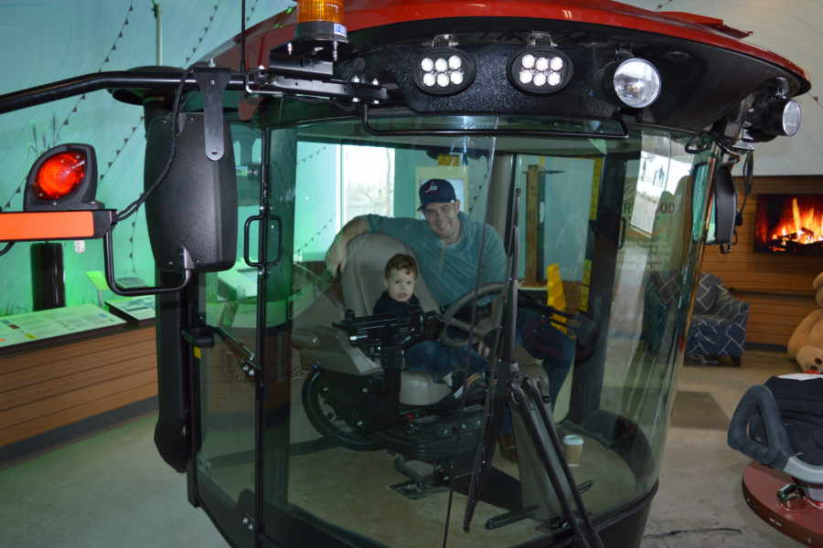 A child and adult sit inside the model swather cab at FFDC. 