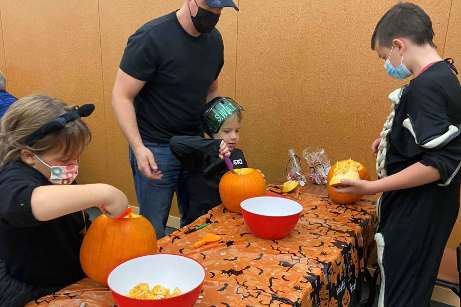 A family carves jack-o-lanterns while wearing costumes during FFDC's Pumpkin Carving Party.