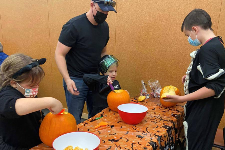 A family carves jack-o-lanterns while wearing costumes during FFDC's Pumpkin Carving Party.