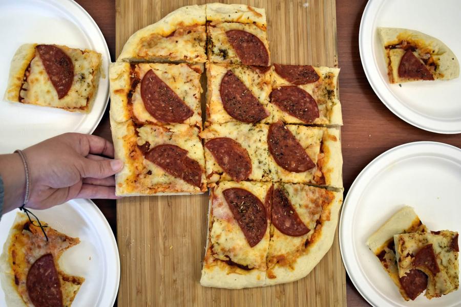 Sliced pizza is displayed on a board, surrounded by pizza slices on plates