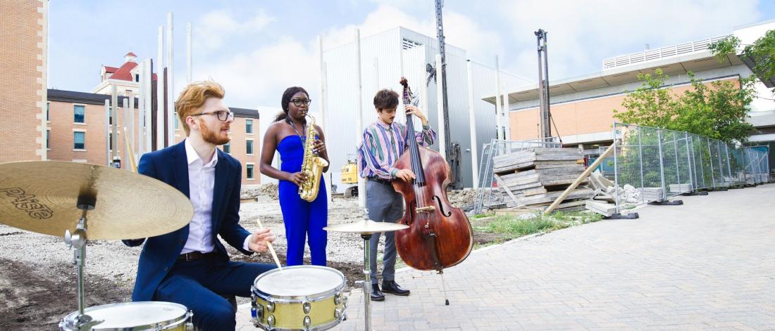 A drummer, saxaphonist and bassist perform at Desautels Concert Hall construction site.