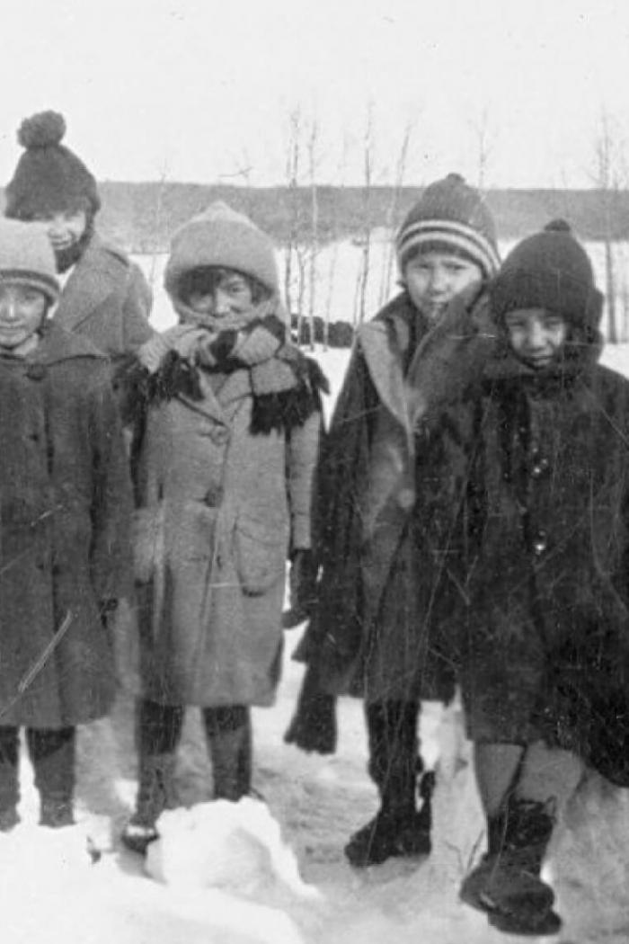 A black and white photo of five small indigenous children huddled together outside in winter.