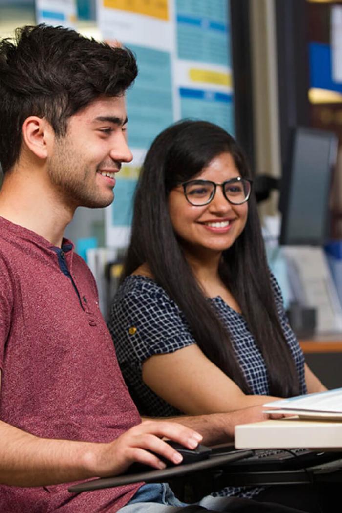 Two students seated at a computer working together. 