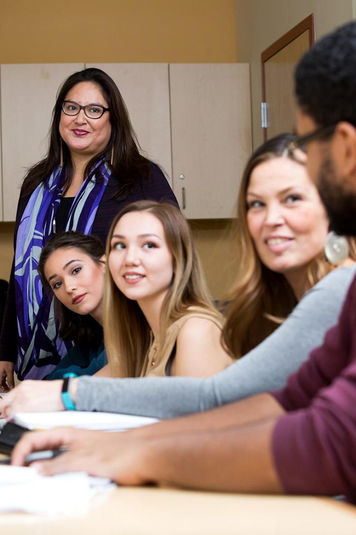 A Qualico bridge to success facilitator, an Indigenous woman stands as she attentively listens to one of the four students seated in front of her.