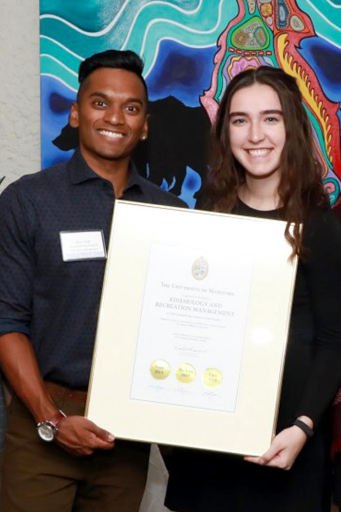 Ryan Singh, a south Asian young male and Ava Glesby, a young Caucasian female stand smiling while holding a framed letter for the student giving program.