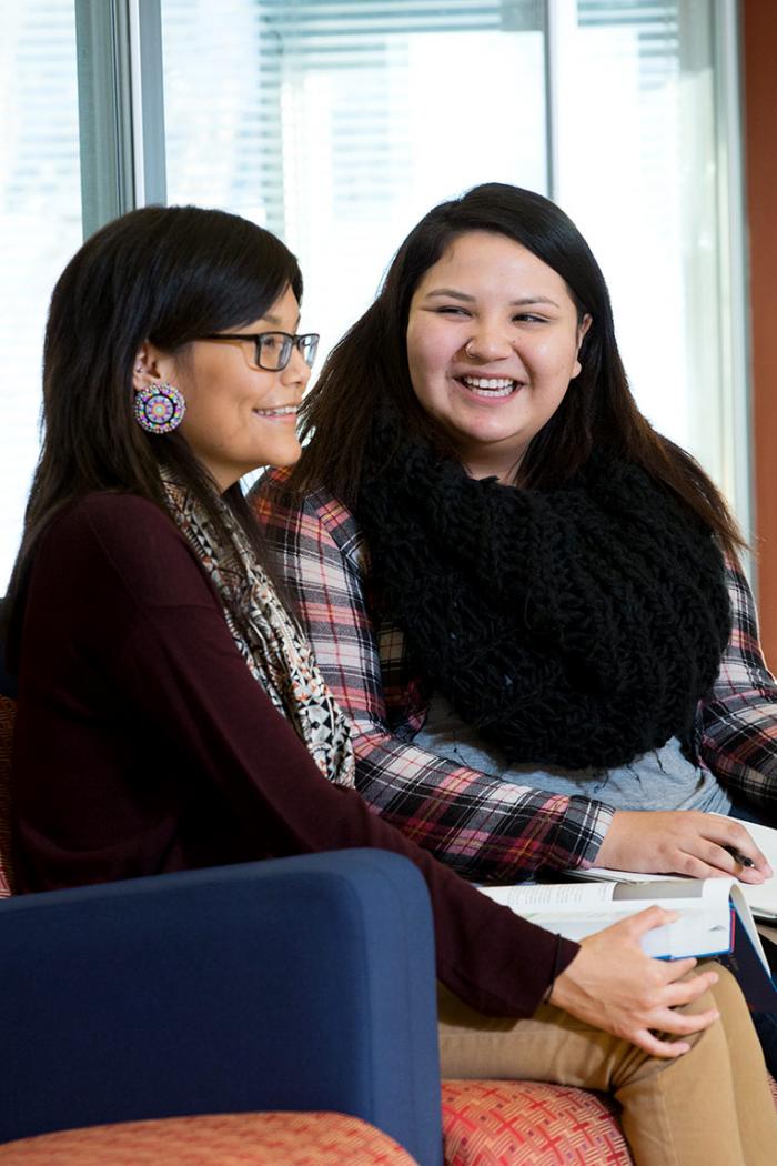 Two young Indigenous women sit smiling in the armchairs in the circle room at Migizii Agamik Bald Eagle Lodge.