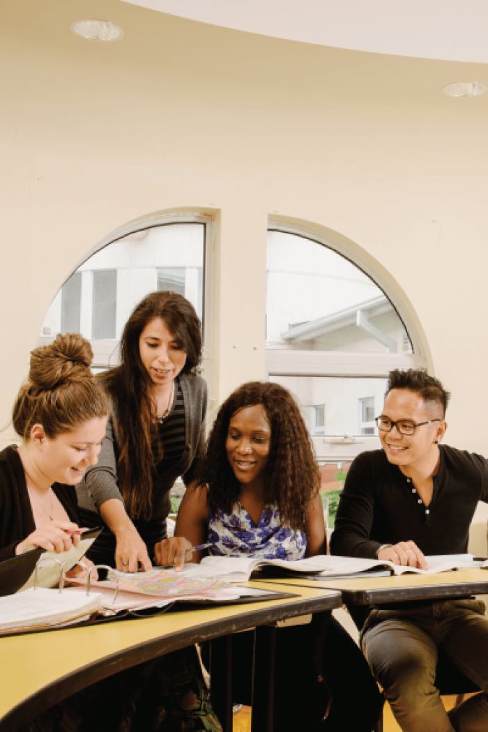 Group of four students in a classroom working at a desk together.