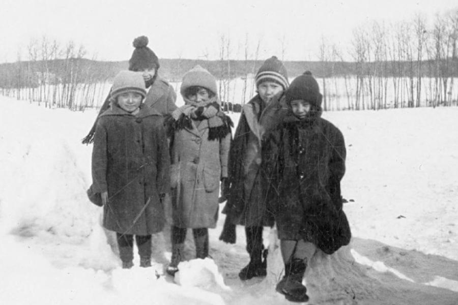 A black and white photo of five small indigenous children huddled together outside in winter.