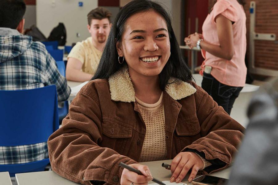 Smiling student with notebook sitting in classroom.