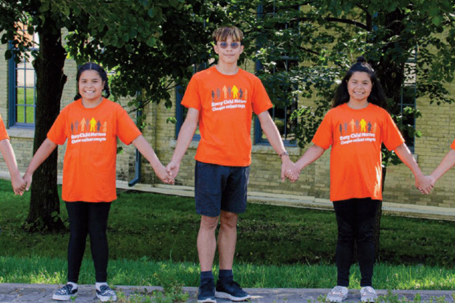 Indigenous children holding hands wearing orange 'every child matters' t-shirts.