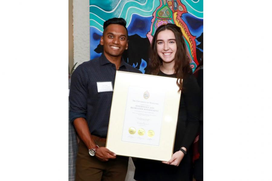 Ryan Singh, a south Asian young male and Ava Glesby, a young Caucasian female stand smiling while holding a framed letter for the student giving program.