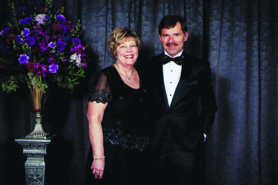 Maggie Katzeley and Barry Konzelman caucasian couple wearing evening attire and beside large flower arrangement