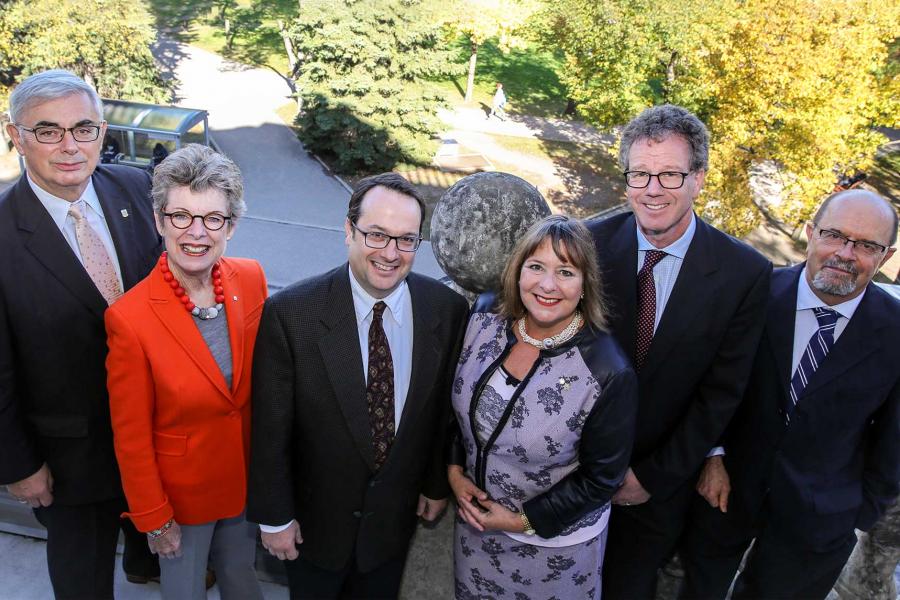 Dr. David Barnard a senior Caucasian male, Susan Glass mature Caucasian female, Bill Kerr Caucasian male, Gail Asper Caucasian female, Michael Paterson Caucasian male and Chris Johnson Caucasian male, standing on an outdoor balcony looking up, with UM building and parks in the background 