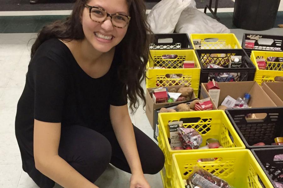 A young woman crouches near a group of milk crates being filled with food items. 
