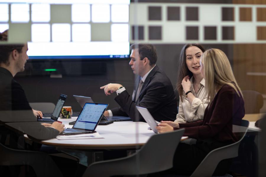 Students wearing suits discuss work in a board room clinic.