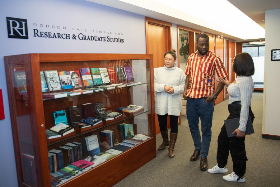 three graduate law students stand by a bookcase in a hallway under a sign that says Research and Graduate Studies