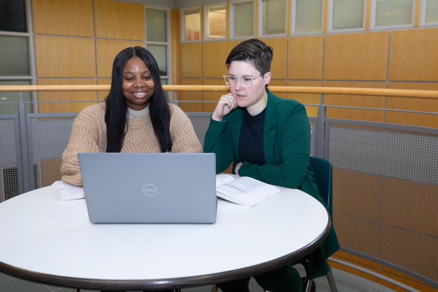 Two people seated at round table looking at a laptop.