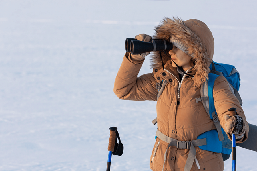 A person wearing a brown coat looking through a binocular.