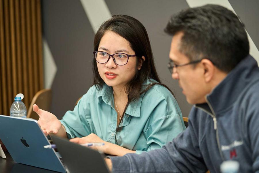 Man and woman in a classroom discussing something that is on a laptop.