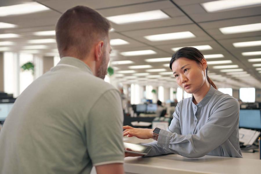 Woman at desk talking to a customer, also using an iPad, while in an office setting.