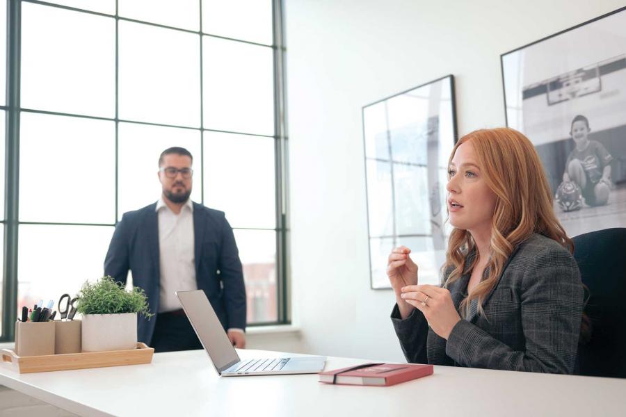Two people in an office meeting, a woman in a suit is leading the conversation.