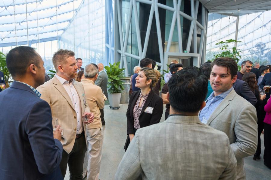 Groups of people networking in an atrium with lots of light and plants.