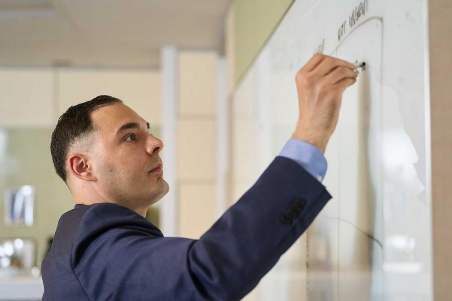 Man in business suit writing on white board.