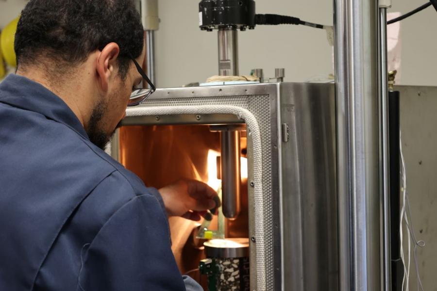 Man with glasses and work shirt with collar leaning over a large engineering lab instrument.