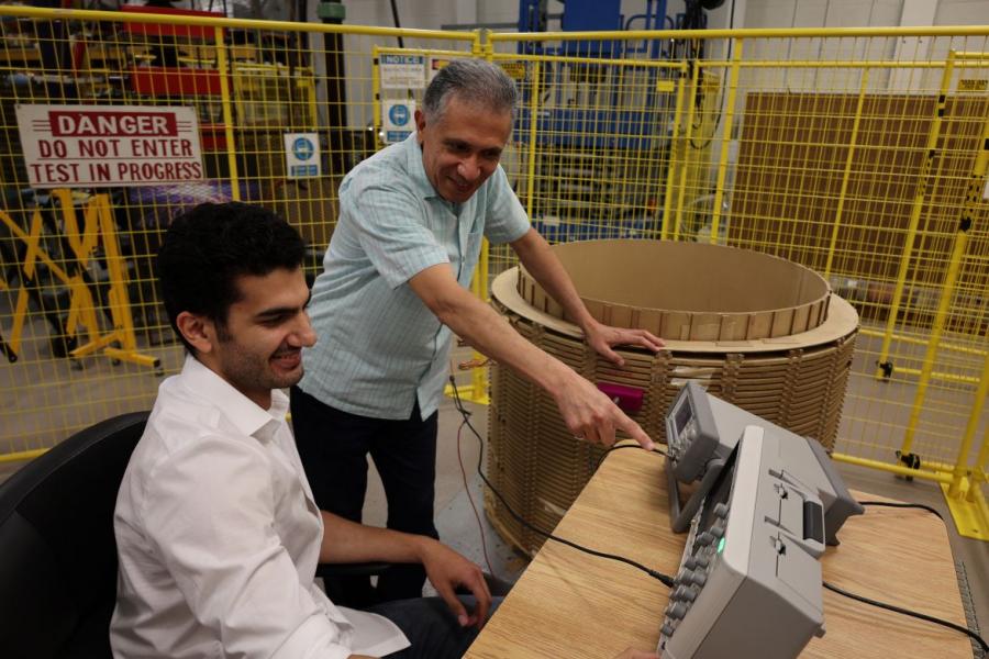 Electrical engineering student sitting at a desk in a warehouse being taught how to use high voltage equipment.