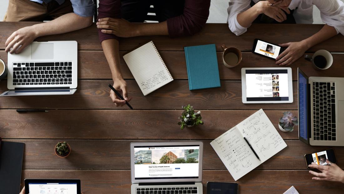 Aerial view of people sitting at a table looking at laptap, mobile and tablet screens