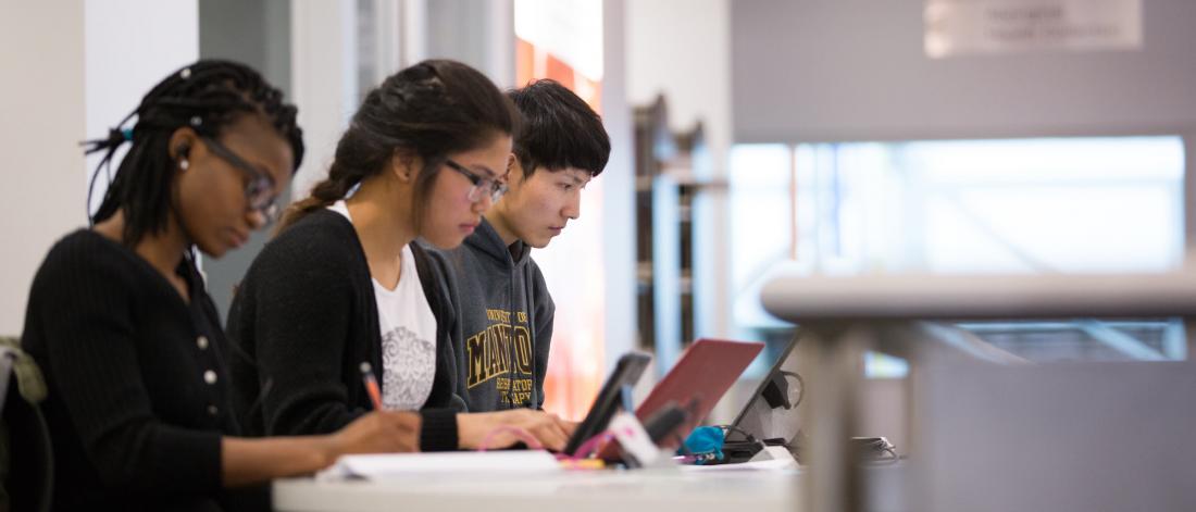 Three students studying and using laptops as a desk in the health sciences library.