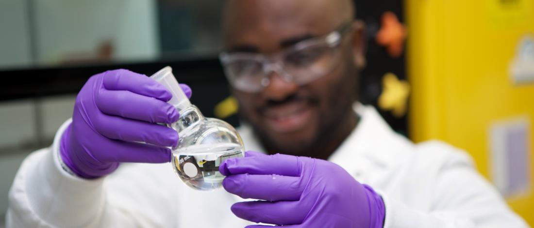 Grad student examining liquid in a glass container.