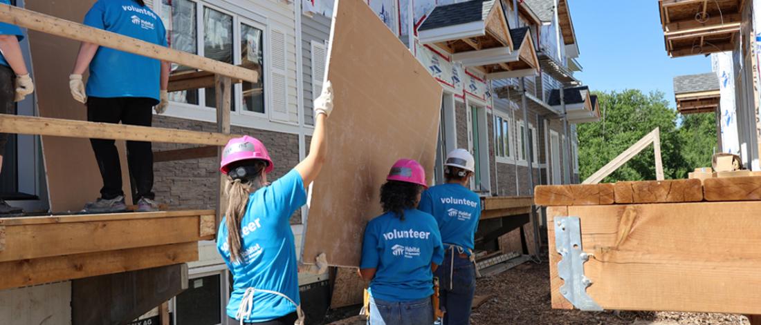 Group of faculty and staff holding carrying a panel at a habitat build site.