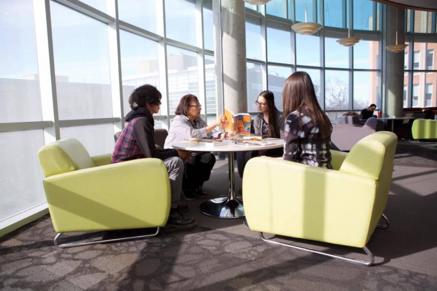 Four people sit around a circular table and look at books together.